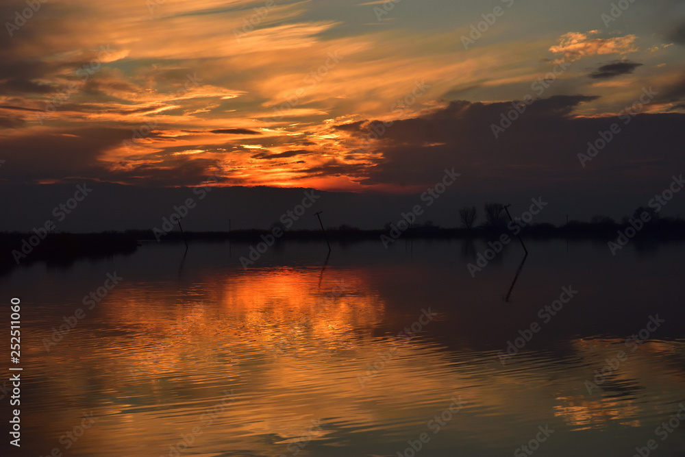 Seashore during sunset with orange reflection on water with a crooked pole in the water