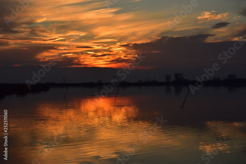 Seashore during sunset with orange reflection on water with a crooked pole in the water