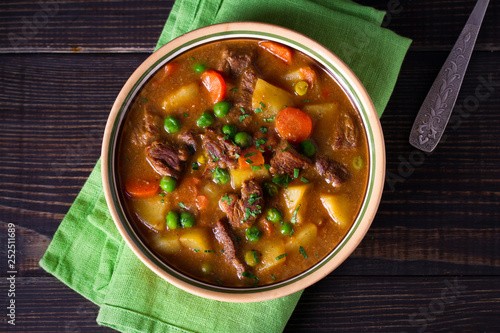 Homemade Irish beef stew with potatoes, carrots and peas in bowl on wooden table. overhead, horizontal photo