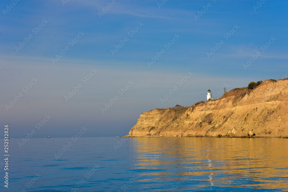 White small lighthouse on cliff by blue Greek sea