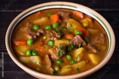 Homemade Irish beef stew with potatoes, carrots and peas in bowl on wooden table. horizontal