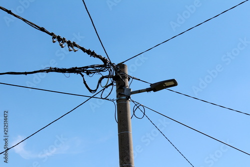 Concrete electrical utility pole with modern LED public light and multiple electrical wires going in all directions on clear blue sky background