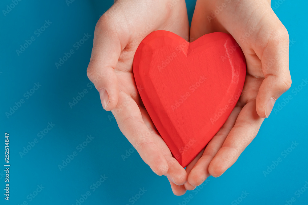 Hands of a teenager child holding a red wooden heart in their hands. Blue background Hands of a teenager child holding a red wooden heart in their hands. Blue background