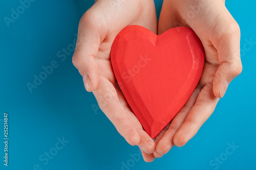 Hands of a teenager child holding a red wooden heart in their hands. Blue background