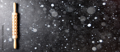 Rolling pin with a pattern in the form of stars on a black board. Baking Background Christmas holidays composition.Concept for Menu, Recipe, Ingredient. Copy space for Text.Drawn Snowfall.Banner