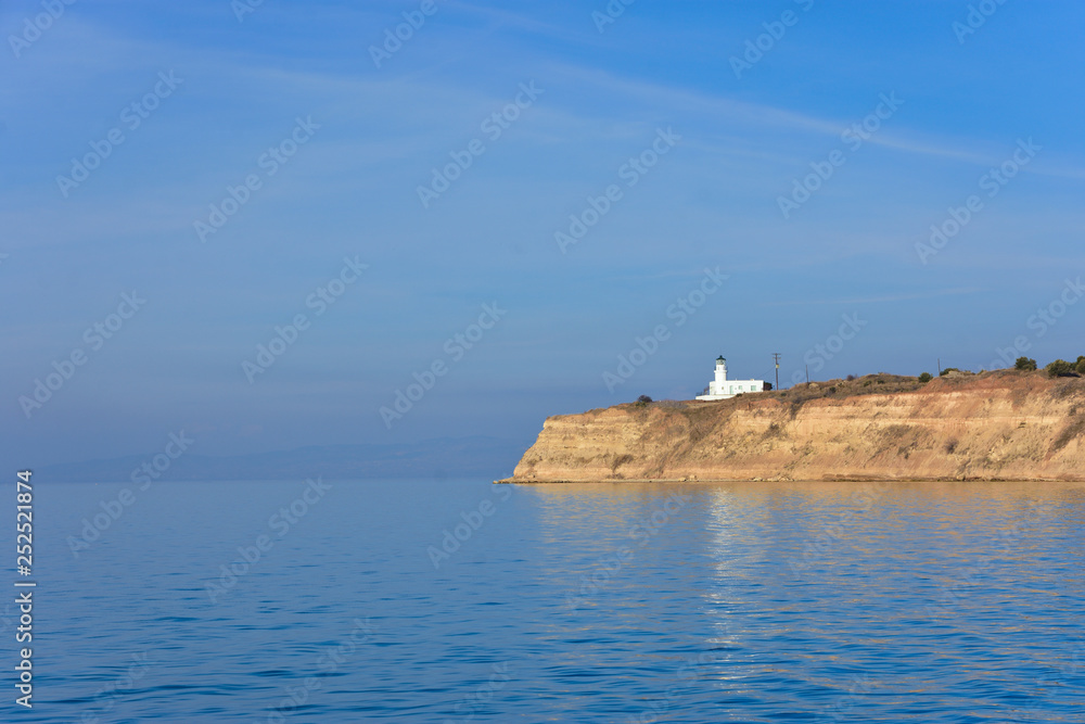 White small lighthouse on cliff by blue Greek sea