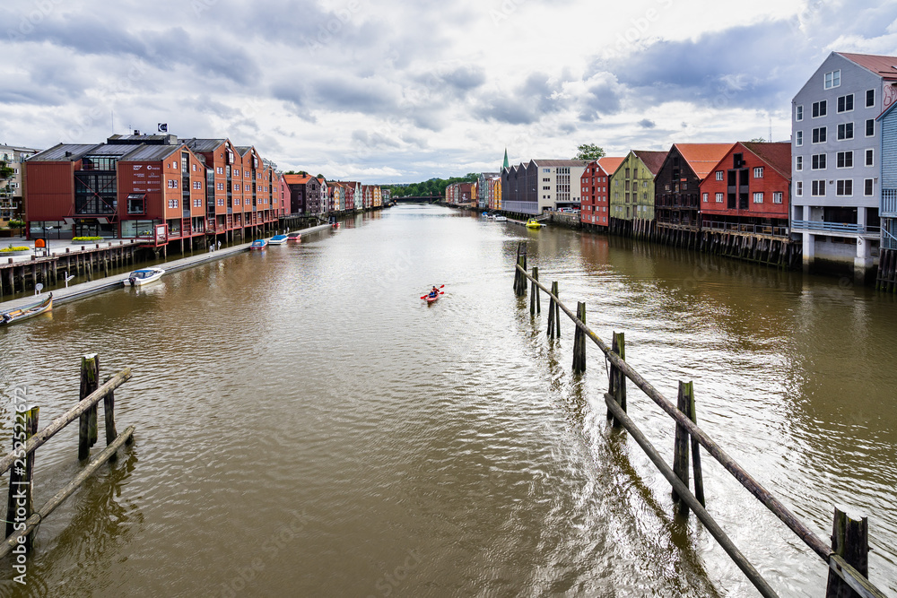 View from Bakke Bru of traditional colorful houses in Trondheim with people canoeing on Nidelva River, Norway