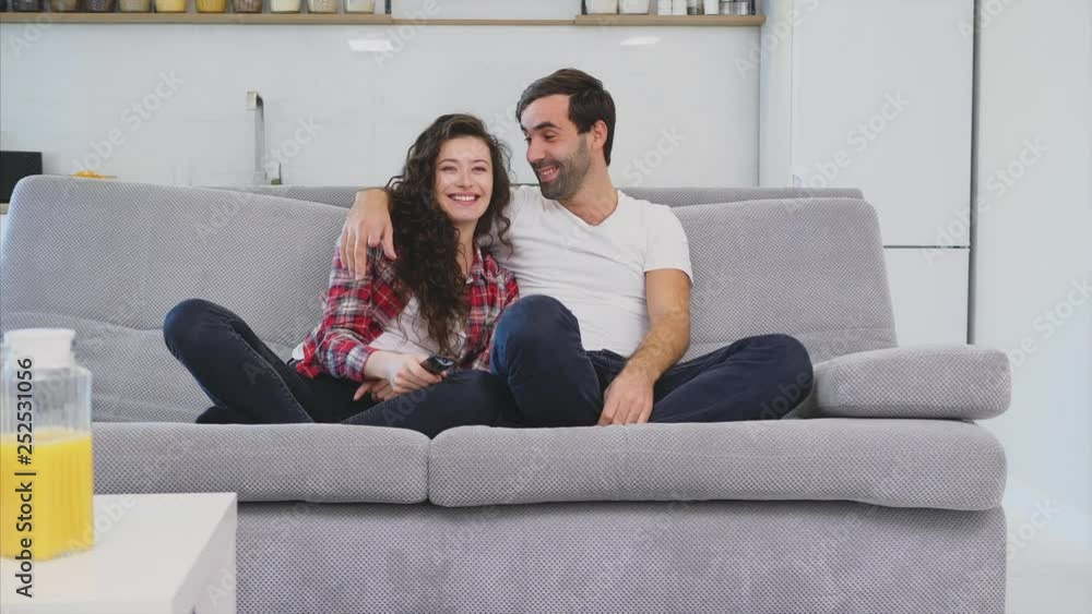 Beautiful girl and a young man sitting on the couch and watch TV. People relax on the couch.Young man in glasses and blue shirt. Beautiful girl and a young man sitting on the couch and watch TV. People relax on the couch.Young man in glasses and blue shirt.