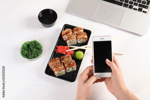Woman with mobile phone and sushi rolls at table, space for text. Food delivery