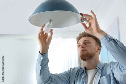 Man changing light bulb in pendant lamp indoors photo