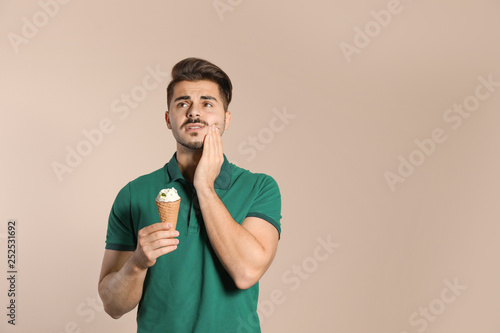 Emotional young man with sensitive teeth and ice cream on color background. Space for text