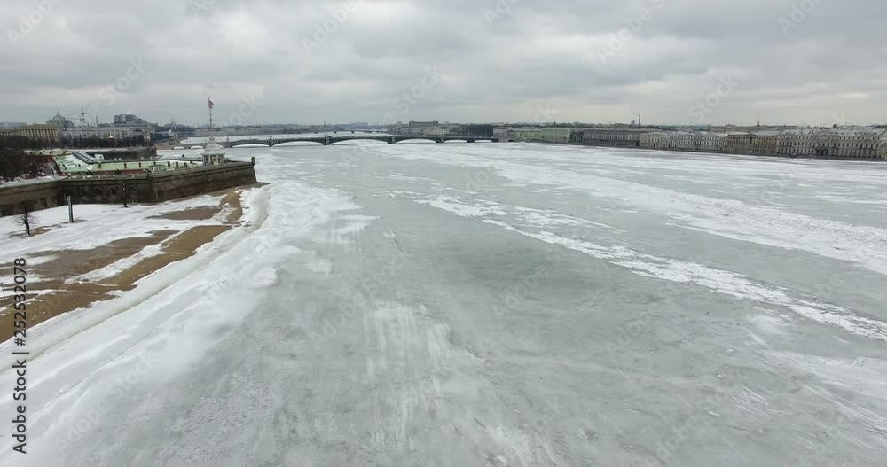 Aerial view. Flying along the river Neva in winter overcast cold weather. Bridge over the river Petersburg. The height of the bird's flight over the frozen river. Aerial view. Flying along the river Neva in winter overcast cold weather. Bridge over the river Petersburg. The height of the bird's flight over the frozen river.