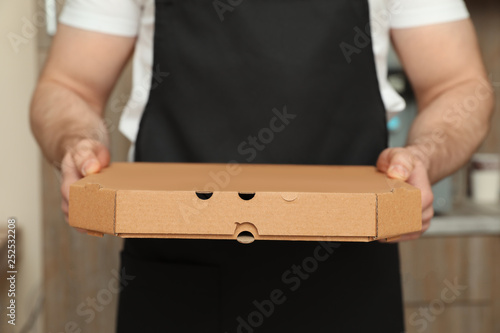 Waiter in apron with pizza box indoors, closeup. Food delivery service © New Africa