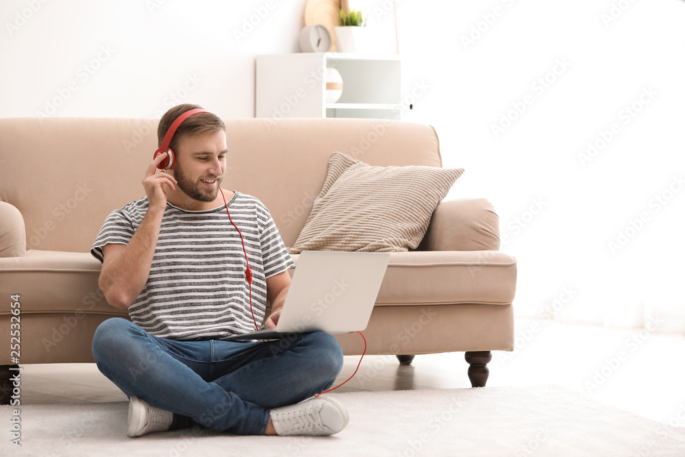 Young man with headphones and laptop sitting on floor in living room Young man with headphones and laptop sitting on floor in living room