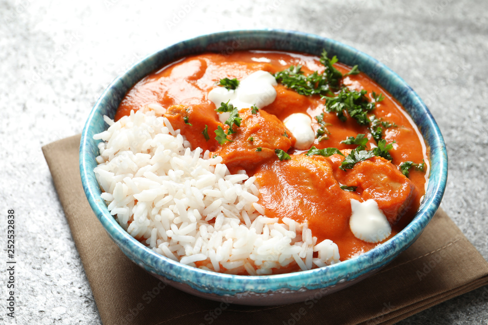 Bowl of butter chicken with rice on grey table