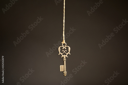 Bronze vintage ornate key hanging on thread against dark background