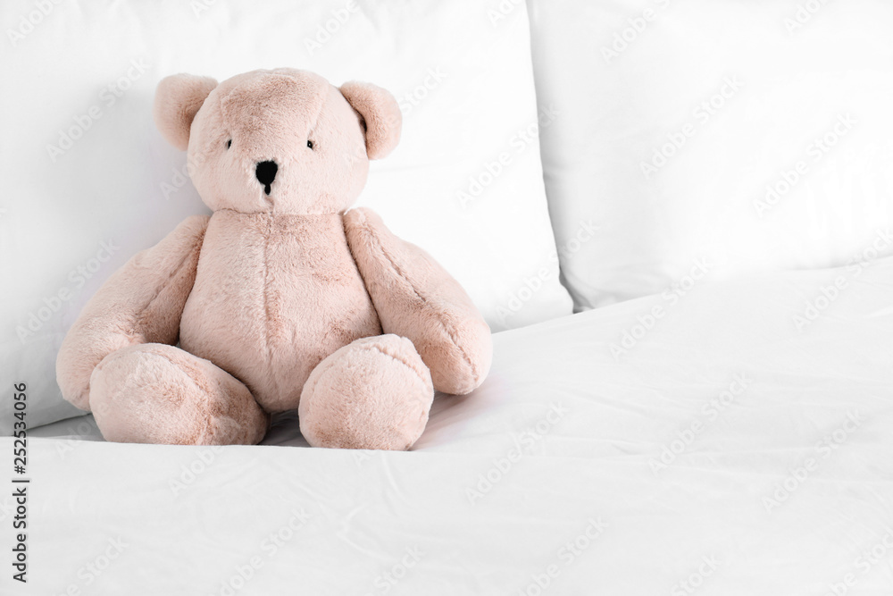Cute teddy bear sitting on bed indoors. Space for text Cute teddy bear sitting on bed indoors. Space for text