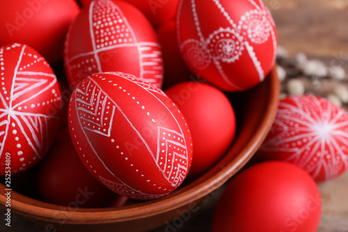 Wooden bowl with red painted Easter eggs on table, closeup