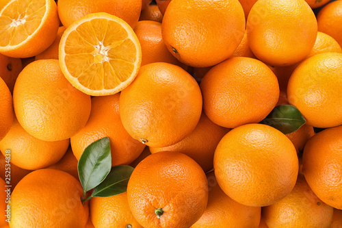 Pile of fresh ripe oranges with leaves as background, top view