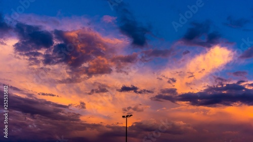 A cloudy orange sunset with the silhouette of a triple head sporting field light