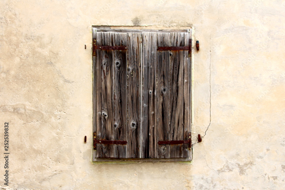 Old wooden window blinds held together with rusted metal hinges mounted on cracked dilapidated house wall on warm sunny day Old wooden window blinds held together with rusted metal hinges mounted on cracked dilapidated house wall on warm sunny day