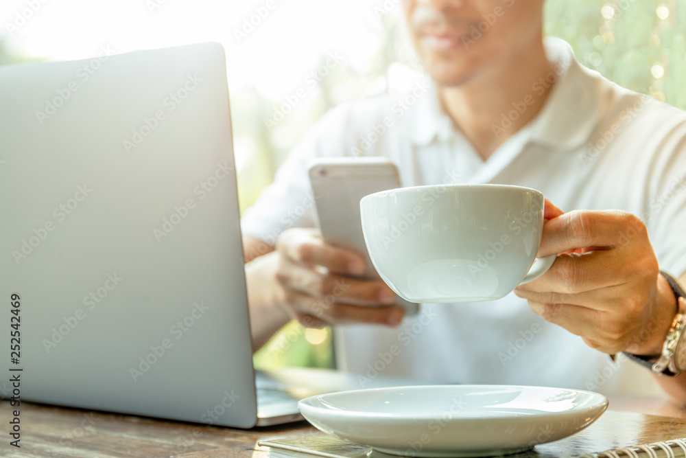 Businessman looking at cell phone with hand holding coffee in coffee shop.