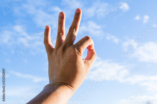 hand showing okay sign against blue sky with clouds