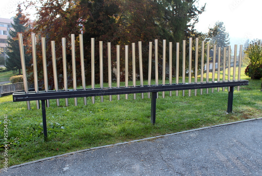 Public installation of musical pipes in various sizes that can be played to simple melody surrounded with paved path and uncut grass on warm sunny day