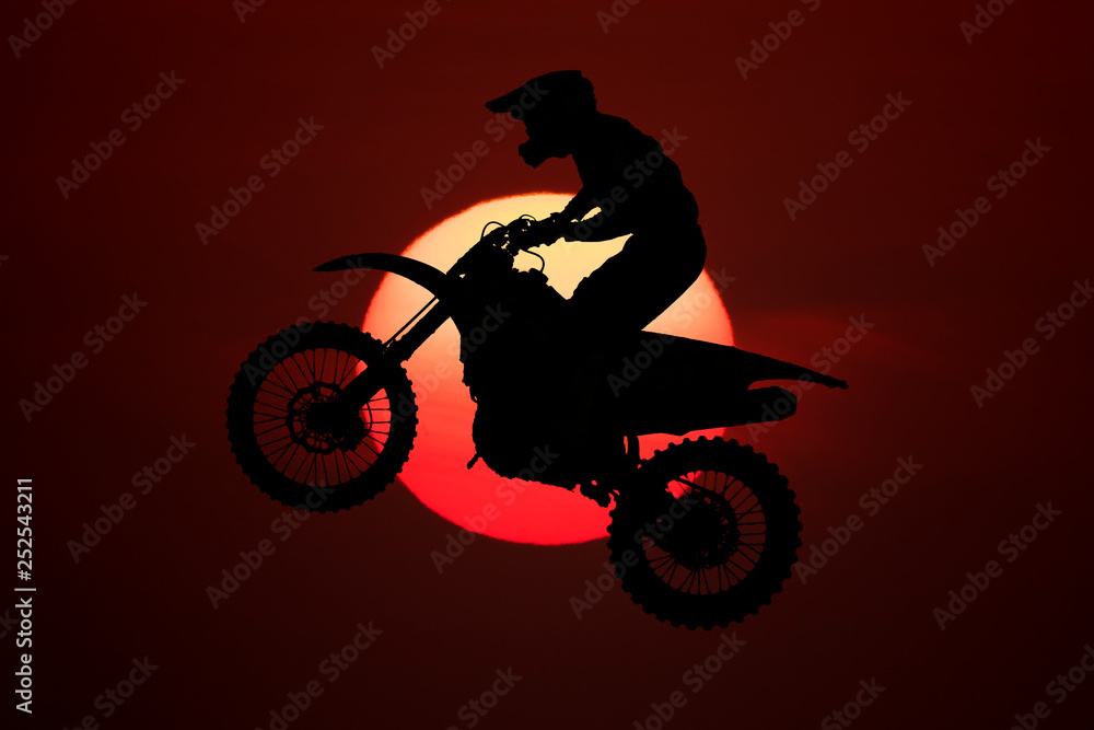 Silhouette of motocross jump in the air with big sun background.