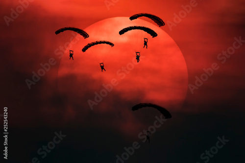Obraz na plátně Five parachutes silhouette in front of big sun with smoke in battle field mood