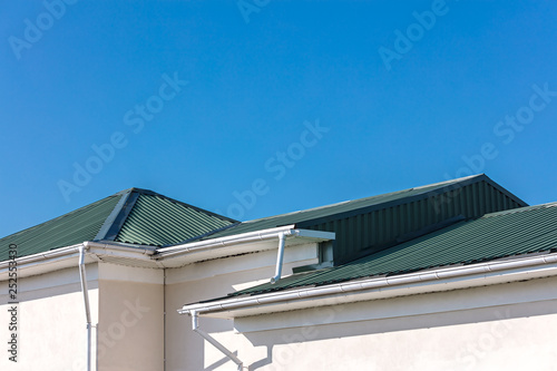 house roof with new gutter system and downspouts on blue sky background