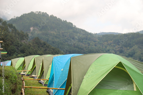 Closeup of camping tents row on green lawn on the hill with tropical mountainous forest background. © Amphon