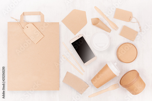 Blank different cardboard packaging for fast food - bag, coffee cup, screen phone, cutlery, sugar, spice, container and box for soup on white wood board.