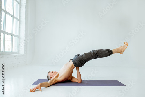 Fototapeta Naklejka Na Ścianę i Meble -  Senior athletic man with naked torso practising yoga poses in the white studio