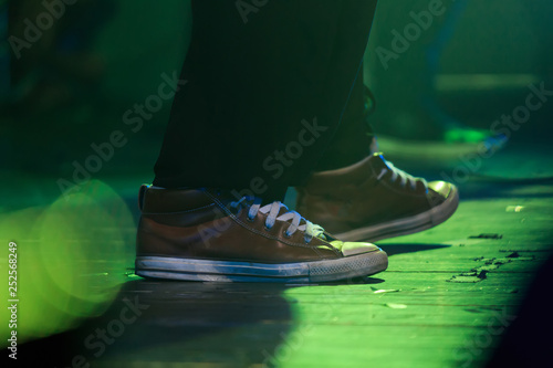 A singer in converse snickers standing on the stage in green light during a concert