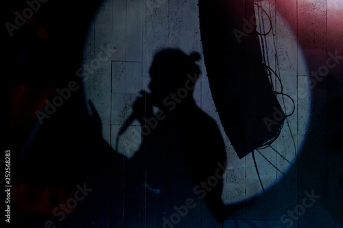 A half-face silhouette of a band singer singing into his microsophone in a round spotlight