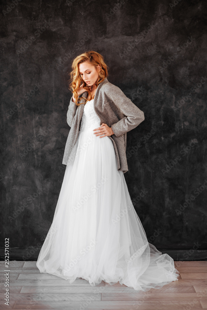 Beautiful smiling blonde woman model in stylish dark overcoat and white dress on dark gray background Beautiful smiling blonde woman model in stylish dark overcoat and white dress on dark gray background