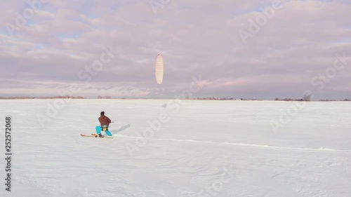 A man is skiing in the snow in a field at sunset. His parachute pulls. Kite surfing in the snow..