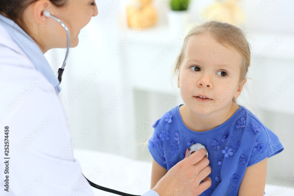 Doctor examining a little girl by stethoscope. Happy smiling child patient at usual medical inspection. Medicine and healthcare concepts