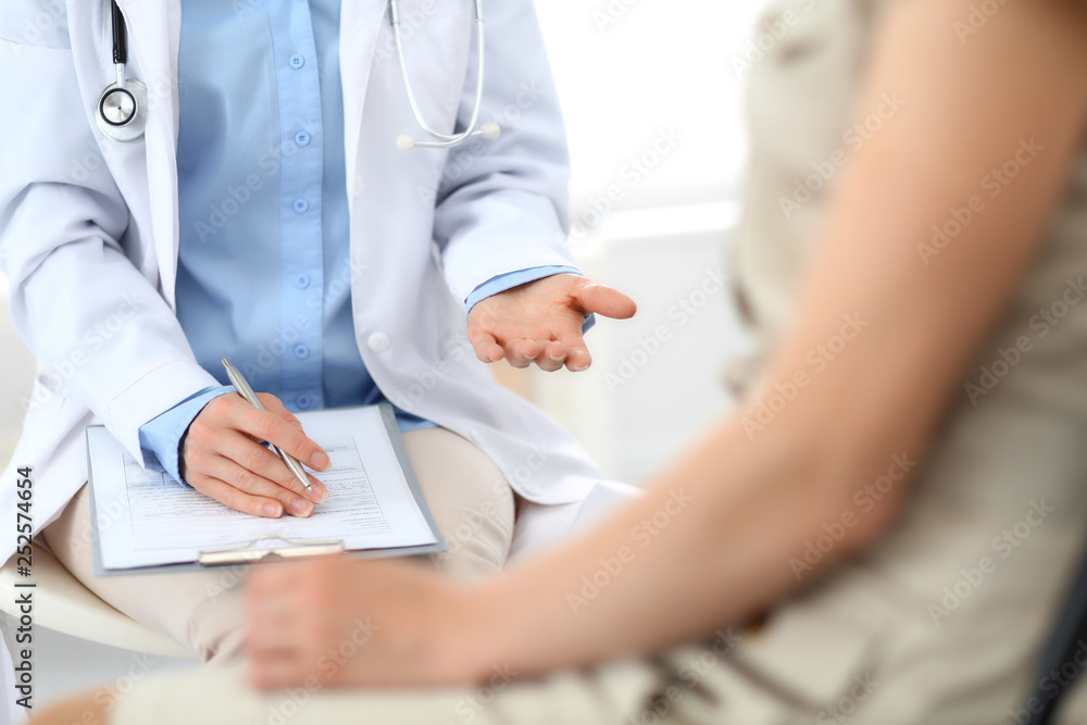 Doctor and patient talking. Physician at work in hospital while writing up medication history records form on clipboard near sitting woman. Healthcare and medicine concepts Doctor and patient talking. Physician at work in hospital while writing up medication history records form on clipboard near sitting woman. Healthcare and medicine concepts