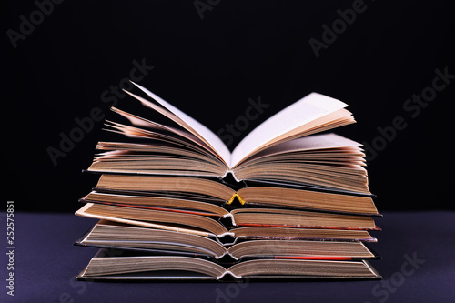 Open books are stacked on the desk, on a black background, isolate. Difficult homework at school, a mountain of knowledge.