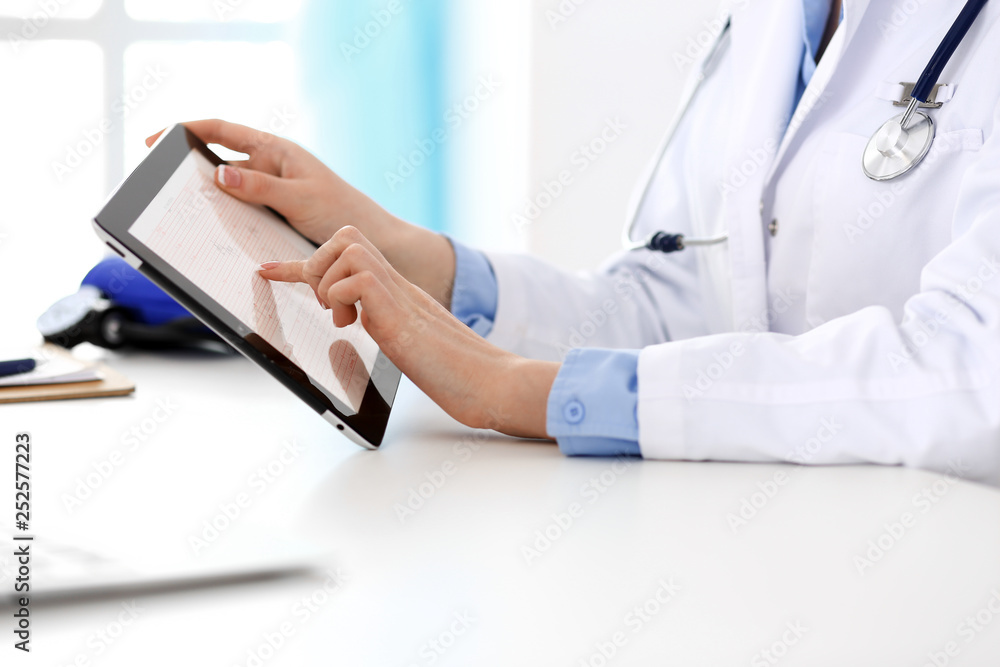 Doctor working table. Woman physician using tablet computer while sitting in hospital office close-up. Healthcare, insurance and medicine concept Doctor working table. Woman physician using tablet computer while sitting in hospital office close-up. Healthcare, insurance and medicine concept