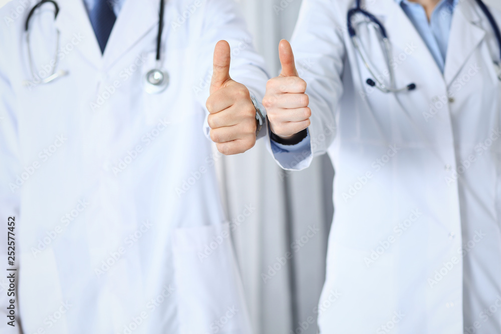 Team of unknown medicine doctors showing OK sign with thumb up close up. Success and high level service in health care, best treatment and customer loyalty and physical concept Team of unknown medicine doctors showing OK sign with thumb up close up. Success and high level service in health care, best treatment and customer loyalty and physical concept