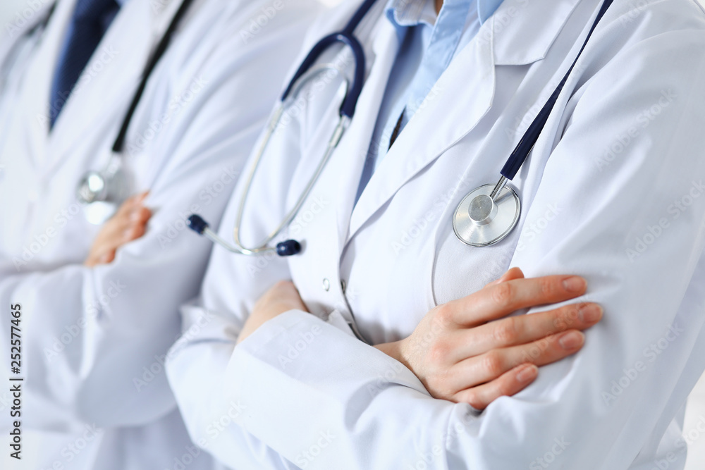 Team of unknown doctors standing straight with arms crossed in hospital. Physicians ready to help. Healthcare, insurance and medicine concept Team of unknown doctors standing straight with arms crossed in hospital. Physicians ready to help. Healthcare, insurance and medicine concept