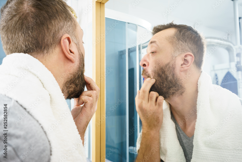 Man looking at his beard in mirror Man looking at his beard in mirror