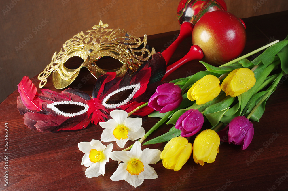 A bouquet of daffodils and tulips, carnival masks on a wooden table