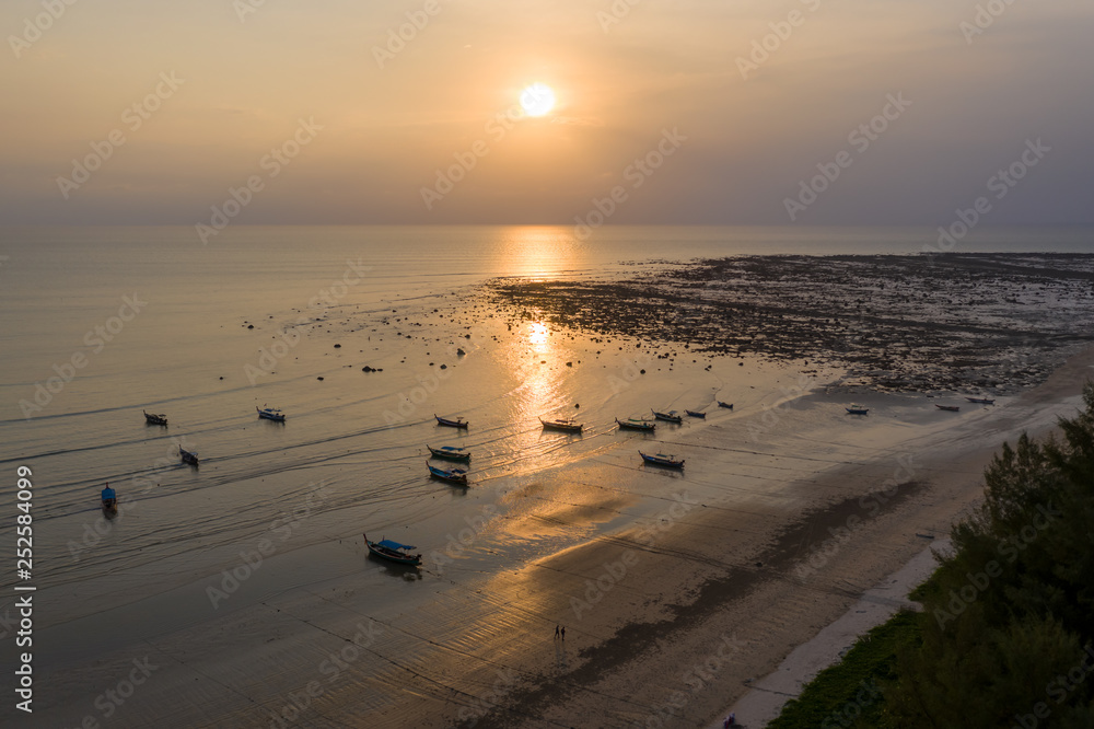 Aerial drone view of sunset over a shallow, tropical ocean with traditional wooden longtail boats at anchor Aerial drone view of sunset over a shallow, tropical ocean with traditional wooden longtail boats at anchor