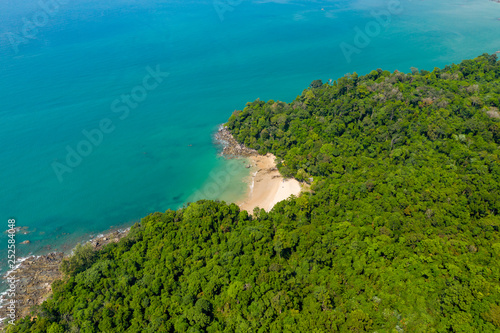 Aerial drone view of a beautiful small sandy beach surrounded by lush, green evergreen forest