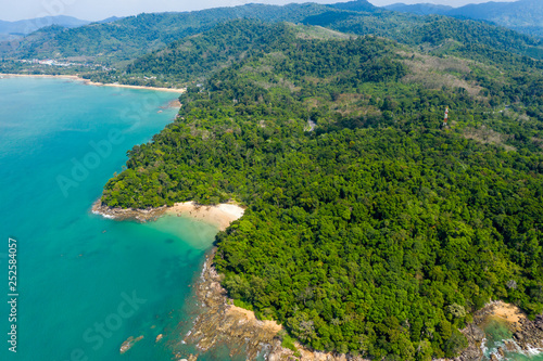 Aerial drone view of a beautiful small sandy beach surrounded by lush, green evergreen forest