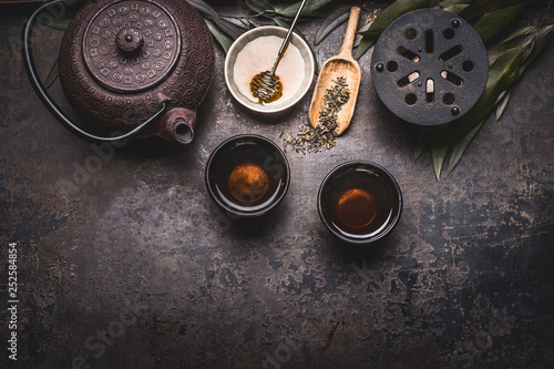 Traditional Asian green tea setting with teapot, cups, candle and honey on dark rustic background with copy space, top view